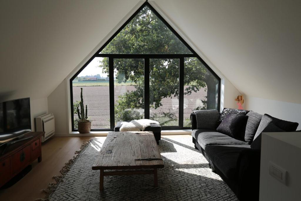 a living room with a couch and a large window at Rozeboom Loft in Aartrijke