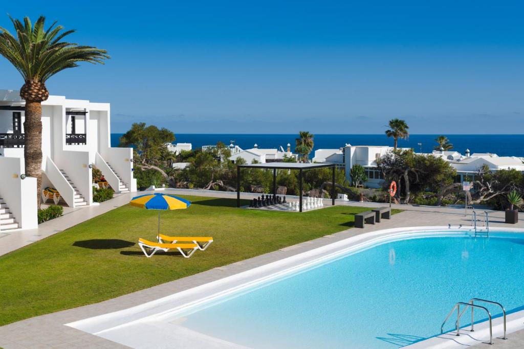 a swimming pool with a table and an umbrella at Charco del Palo apartments en complejo nudista FKK nudist resort Castillo de Papagayo in Charco del Palo