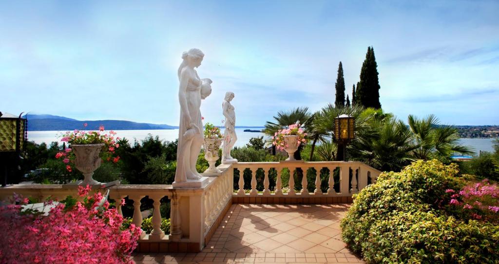 een tuin met beelden op een hek en bloemen bij Park Hotel Ville Montefiori in Gardone Riviera