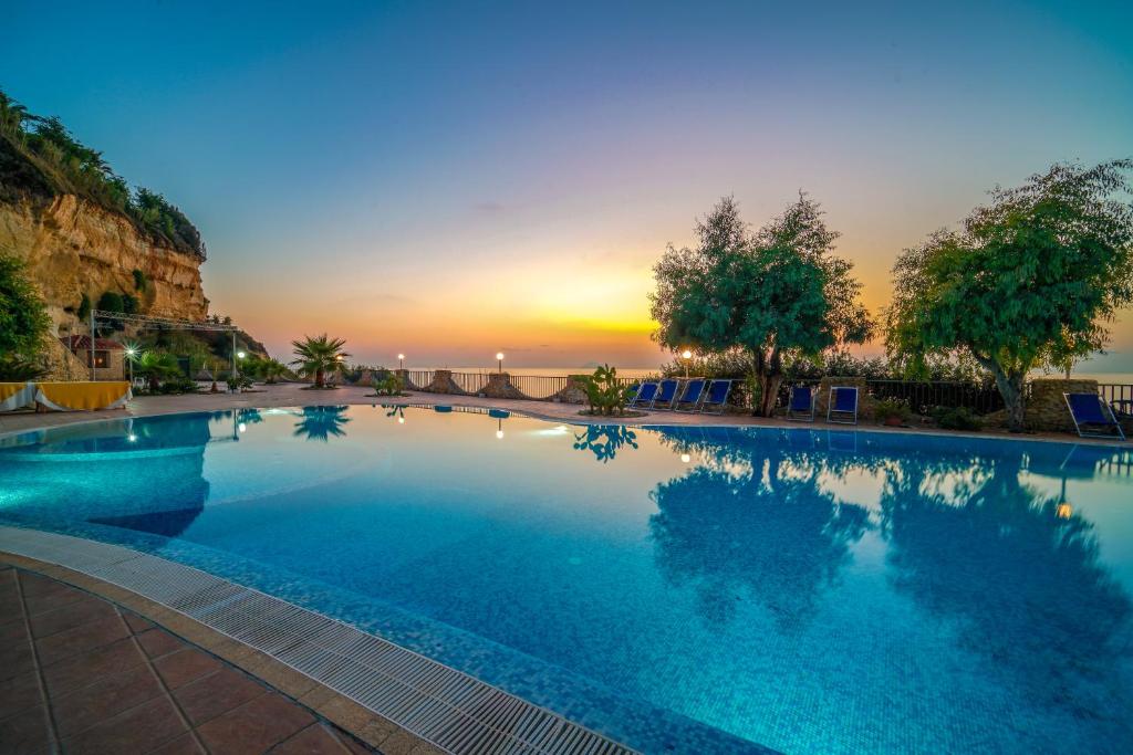 a large swimming pool with a sunset in the background at Villaggio Marco Polo in Santa Domenica