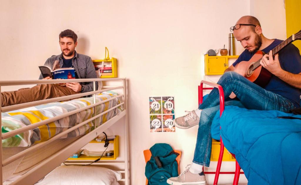 two men are sitting on bunk beds playing guitar at Hostel Il Nosadillo - Bologna in Bologna