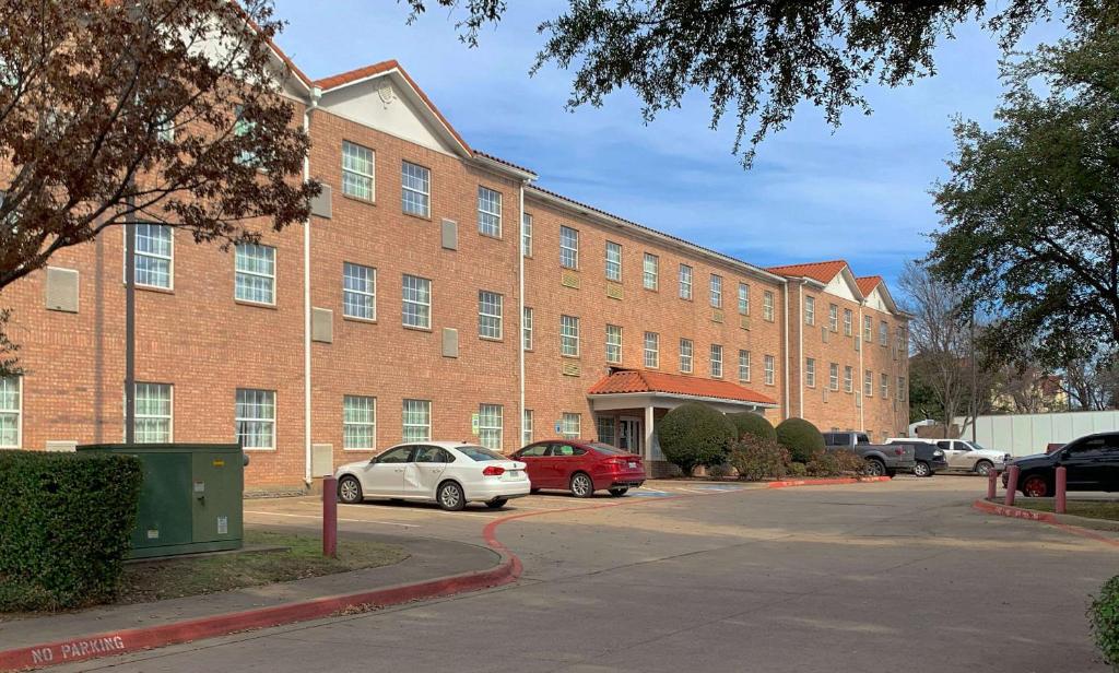 ein großes Backsteingebäude mit Autos auf einem Parkplatz in der Unterkunft MainStay Suites Addison - Dallas in Addison