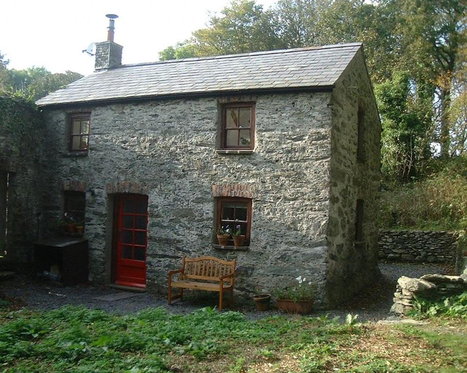 a stone house with a red door and a bench at Gardeners Cottage in Llanrhyddlad