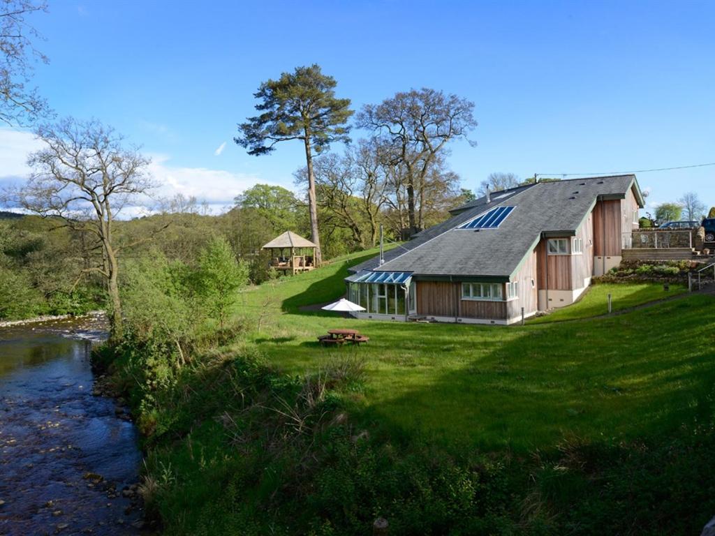 a house on a grass field next to a river at Black Burn Lodge B & B in Newcastleton