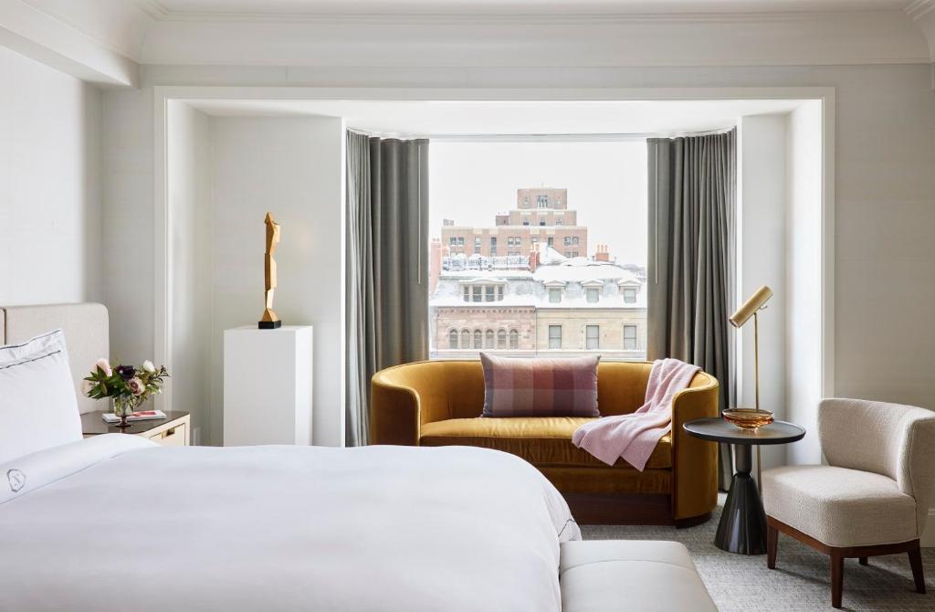 ボストンにあるThe Newbury Bostonのベッド1台、椅子、窓が備わる客室です。