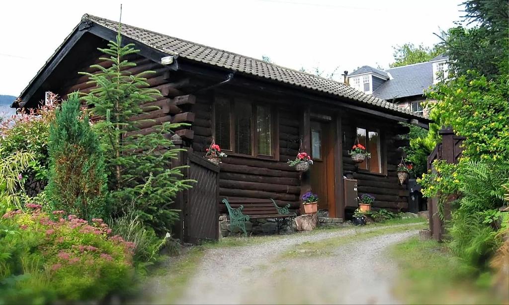 An Carraig Log Cabin في ستراثير: كابينة خشب بها زهور في النافذة