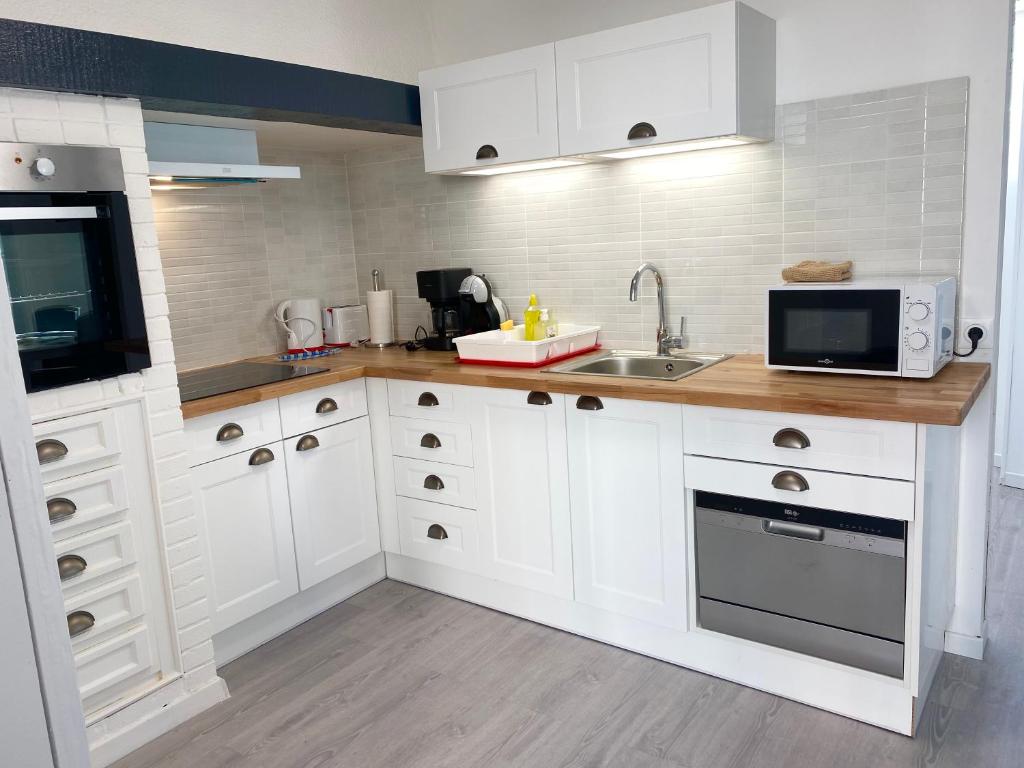a kitchen with white cabinets and a sink and a microwave at L’Abri Côtier in Le Tréport