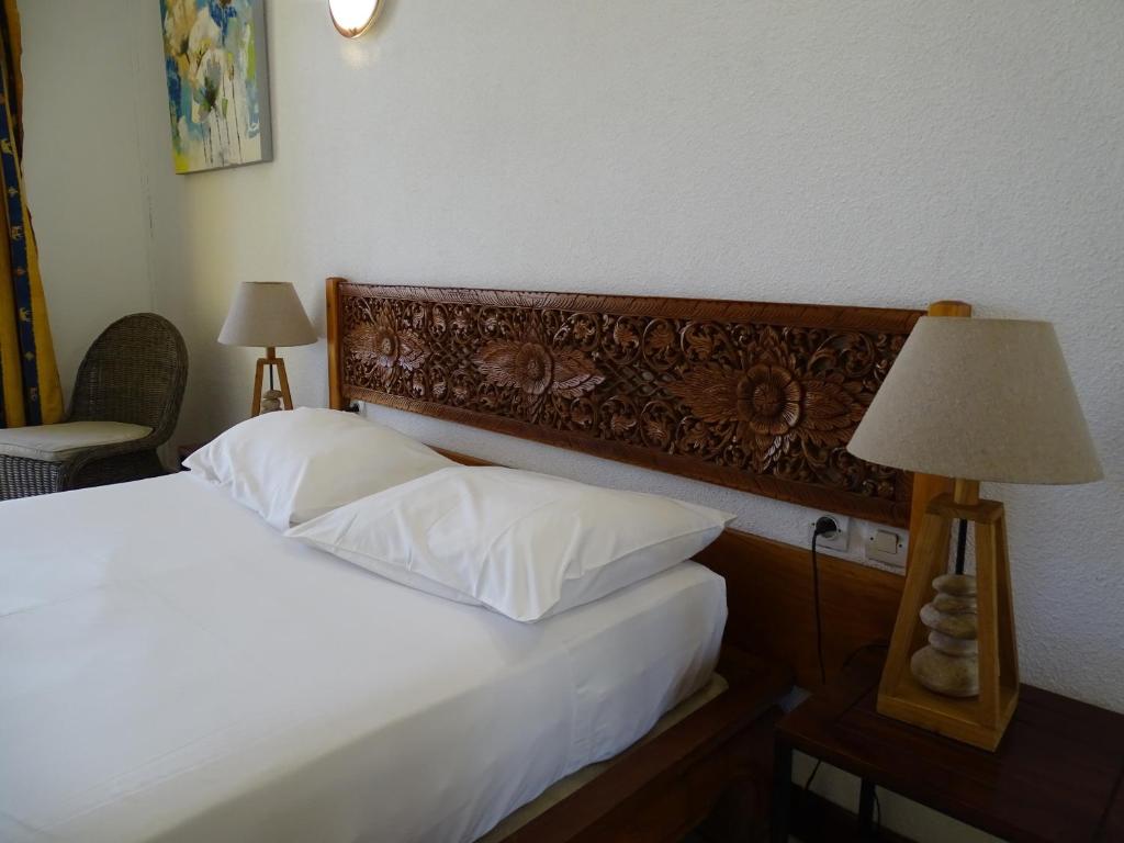 a bedroom with a bed with a wooden headboard and a lamp at Hôtel Résidence Le Phoenix in Saint-Pierre