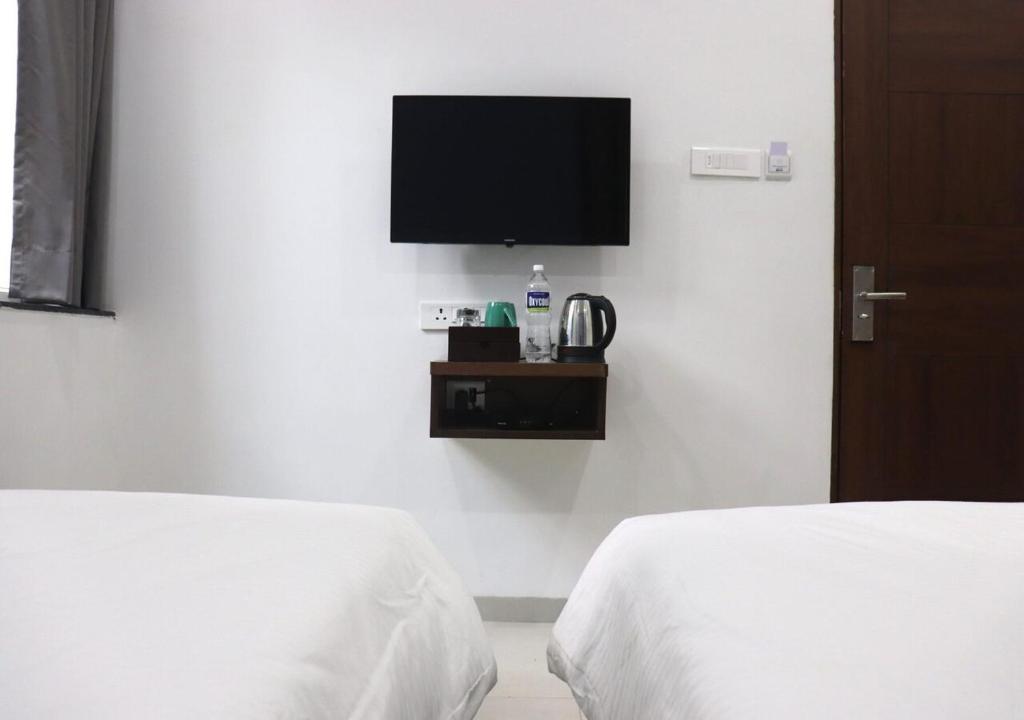 a bedroom with two beds and a tv on the wall at Sharman Suites in Pune