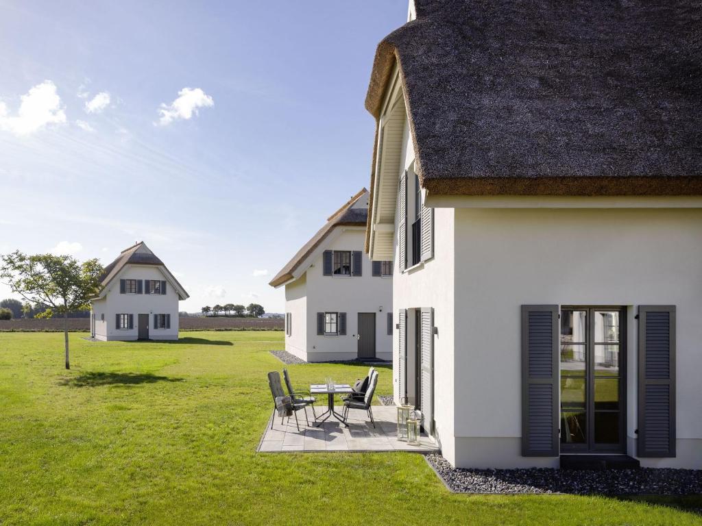 uma casa branca com cadeiras e uma mesa num campo em Reetland am Meer - Superior Reetdachvilla mit 2 Schlafzimmern E14 em Dranske
