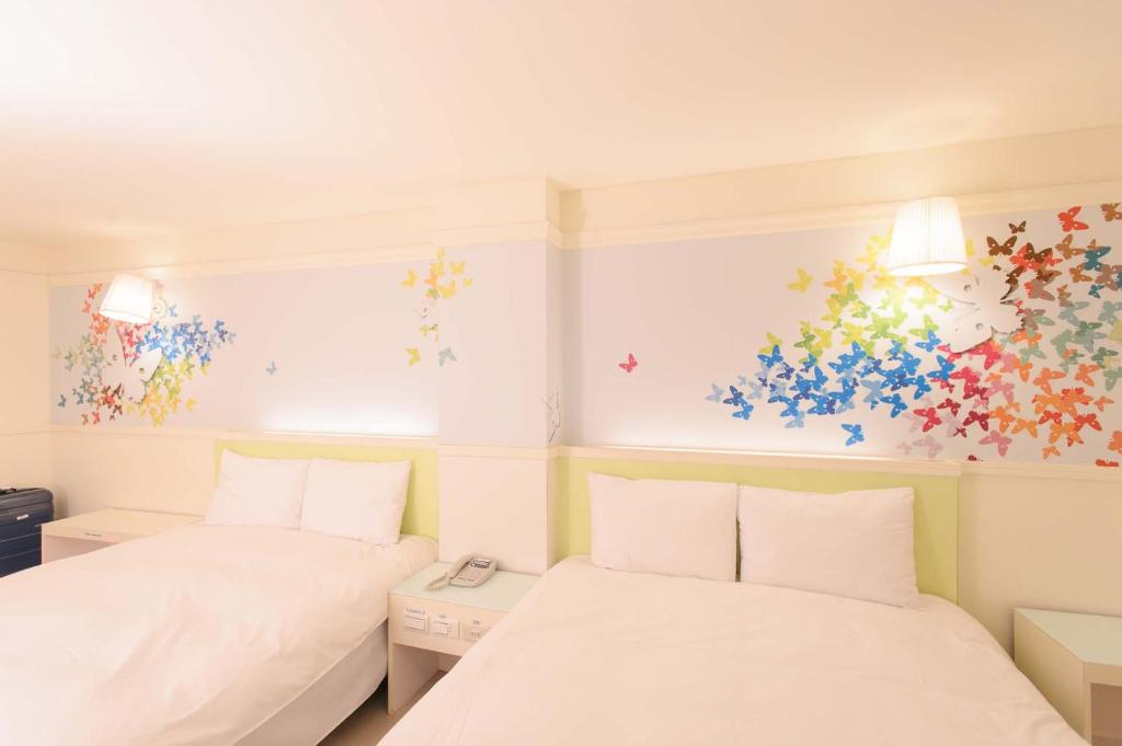 two beds in a room with colorful paintings on the walls at Kiwi Express Hotel - Zhong Zheng Branch in Taichung