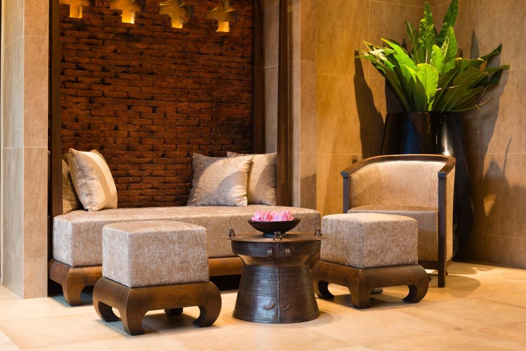 A styled lounge corner with a sofa, armchair, ottomans, and flower-topped table.