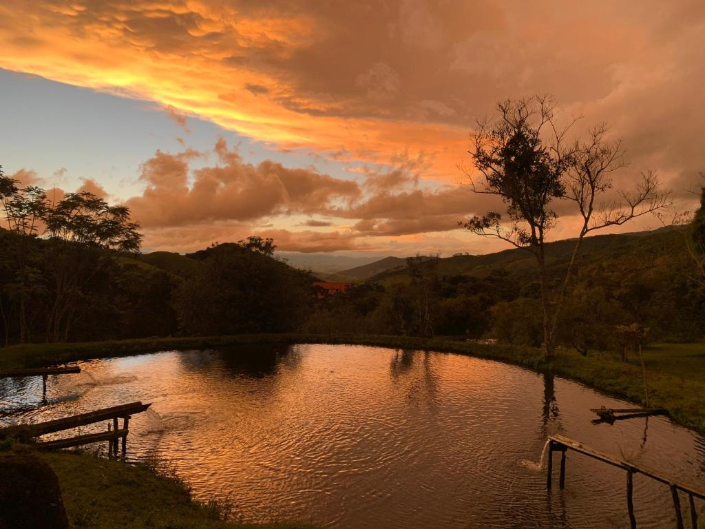 einen Sonnenuntergang über einem Teich mit einer Bank davor in der Unterkunft Delirius Hospedagem in Itamonte