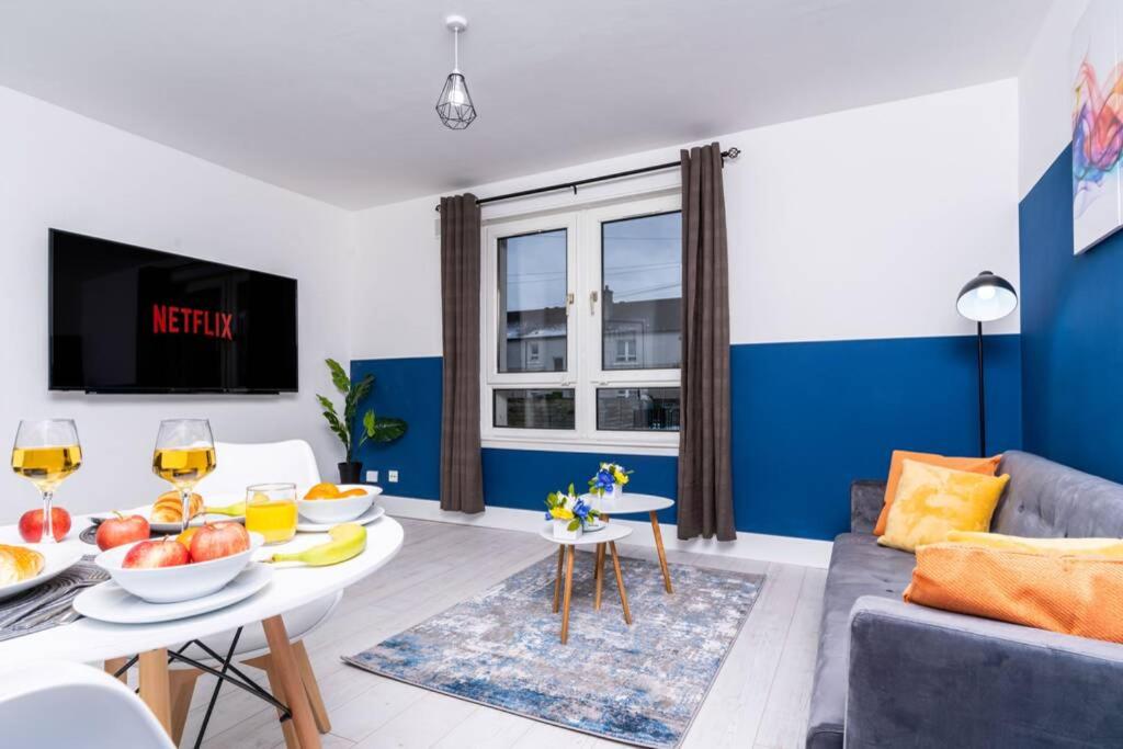ein Wohnzimmer mit einem Tisch mit Obst und Weingläsern in der Unterkunft Cheerful 2 Bedroom Homely Apartment, Sleeps 4 Guest Comfy, 1x Double Bed, 2x Single Beds, Free Parking, Free WiFi, Suitable For Business, Leisure Guest, Contractors, QE Hospital, Glasgow, Near Airport & City Centre in Glasgow