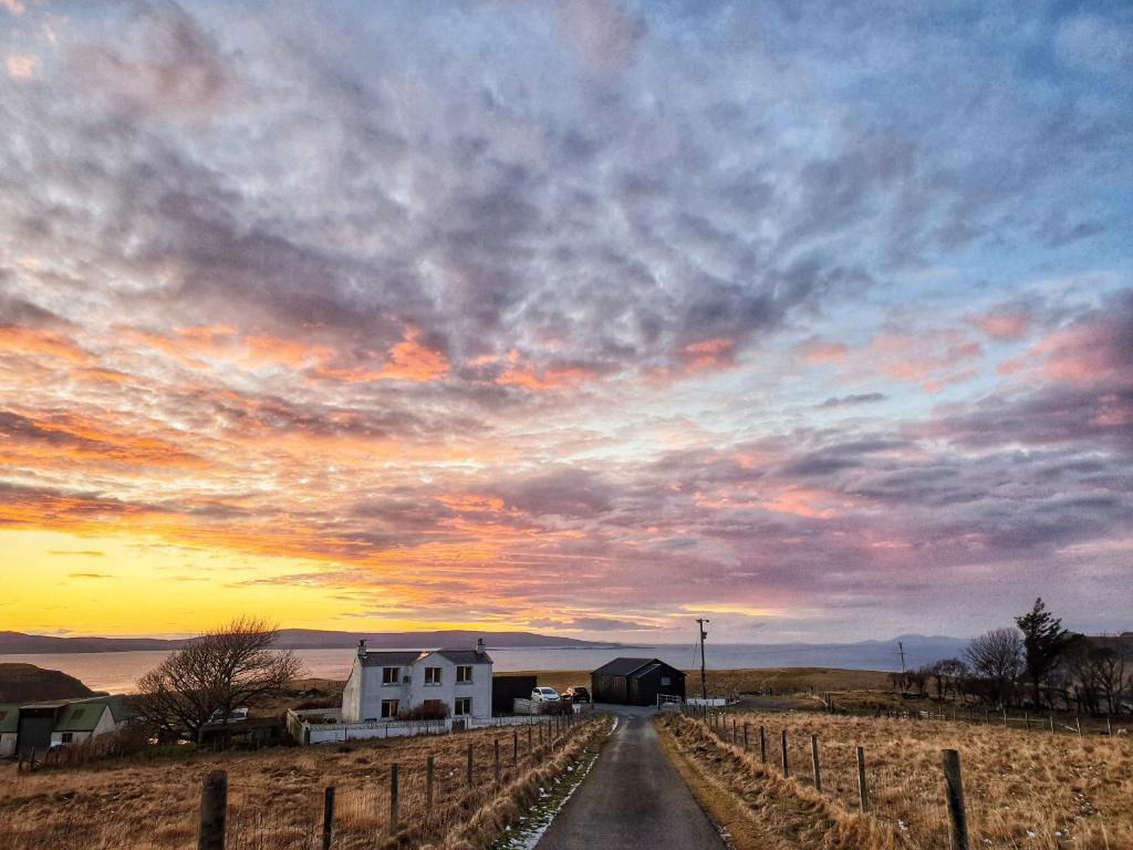 a country road with a farm house and a sunset at Abhaig Boutique B&B - Small & luxurious in a great location! in Uig