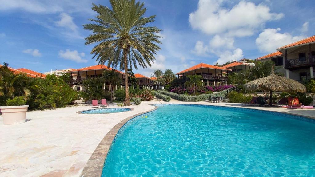a swimming pool in front of a resort with a palm tree at Blue Bay Villa Bon Bini. in Willemstad