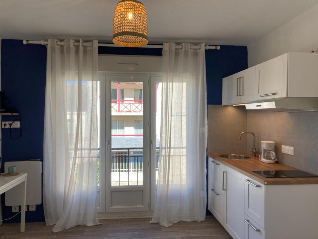 uma cozinha com cortinas brancas e uma porta com uma janela em La Capitane em La Baule