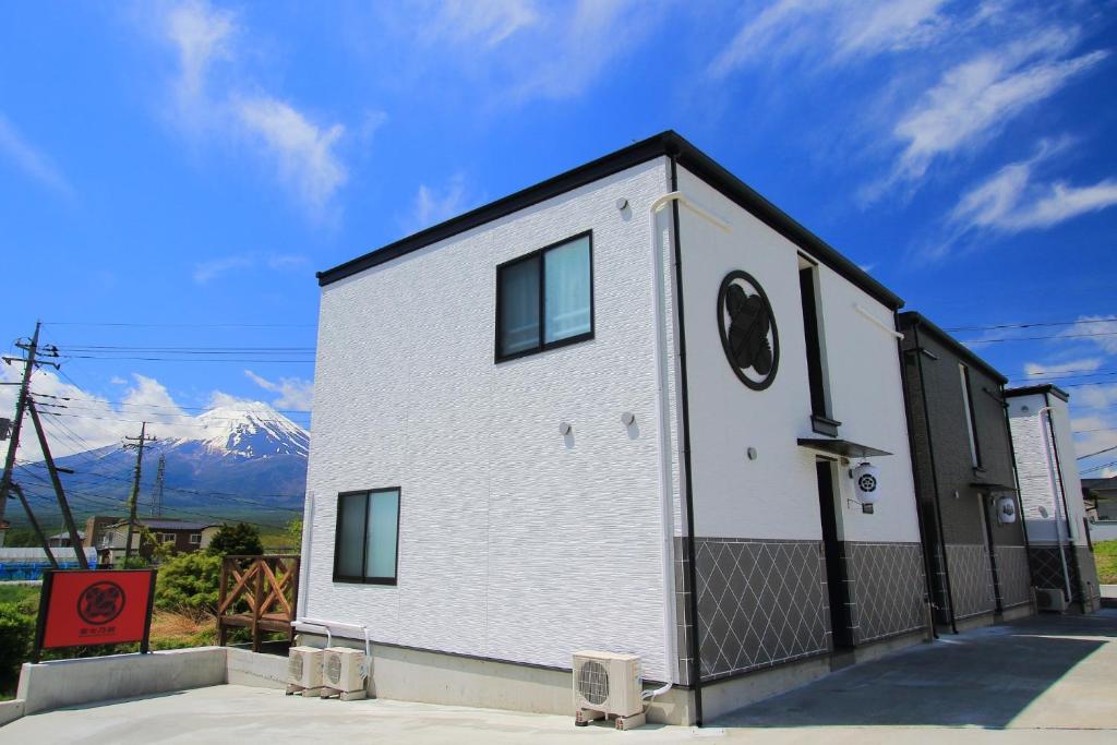 um pequeno edifício branco com montanhas ao fundo em Fujinokura Village C - Vacation STAY 84872 em Fujikawaguchiko