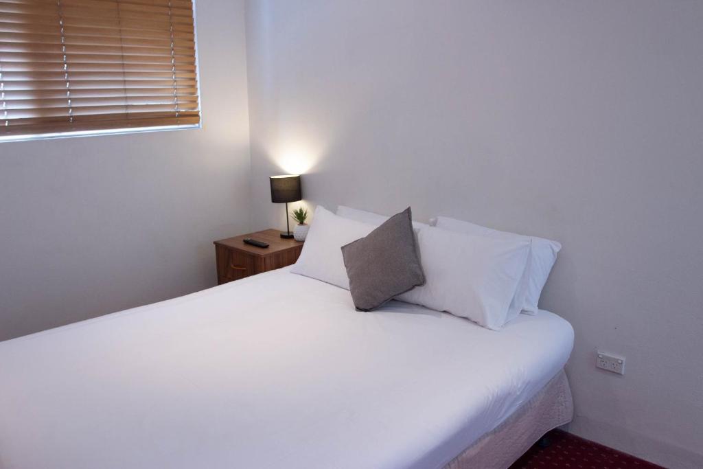 1 cama con sábanas blancas y almohadas en una habitación en Wiley Park Hotel, en Sídney