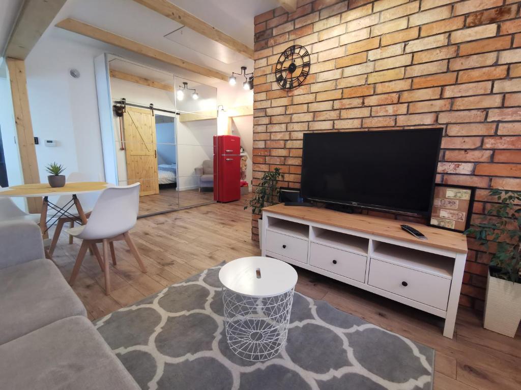 a living room with a tv and a brick wall at Apartament ALPa Kudowa Zdrój in Kudowa-Zdrój