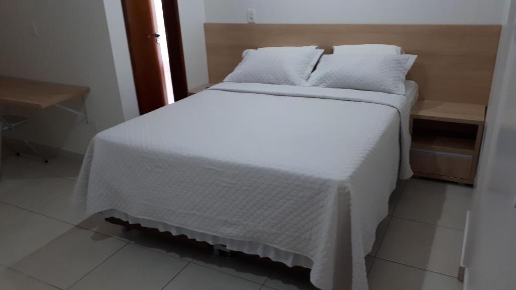 1 cama con sábanas blancas y almohadas en una habitación en Hotel Friburgo, en Cidade Ocidental