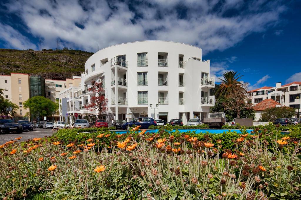 a white building with a flower garden in front of it at White Waters Hotel in Machico