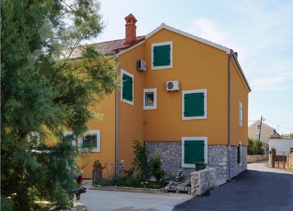 ein großes gelbes Haus mit grünen Rollläden in der Unterkunft Apartments Stosa - with parking in Nin