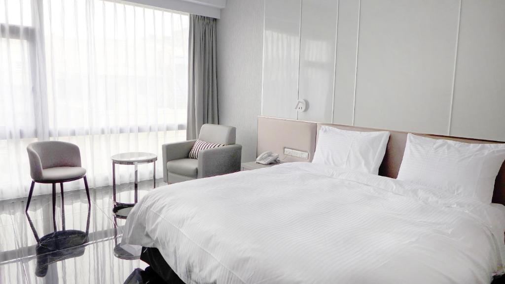 a bedroom with a large white bed and a chair at Champ De Rose Hotel in Hualien City