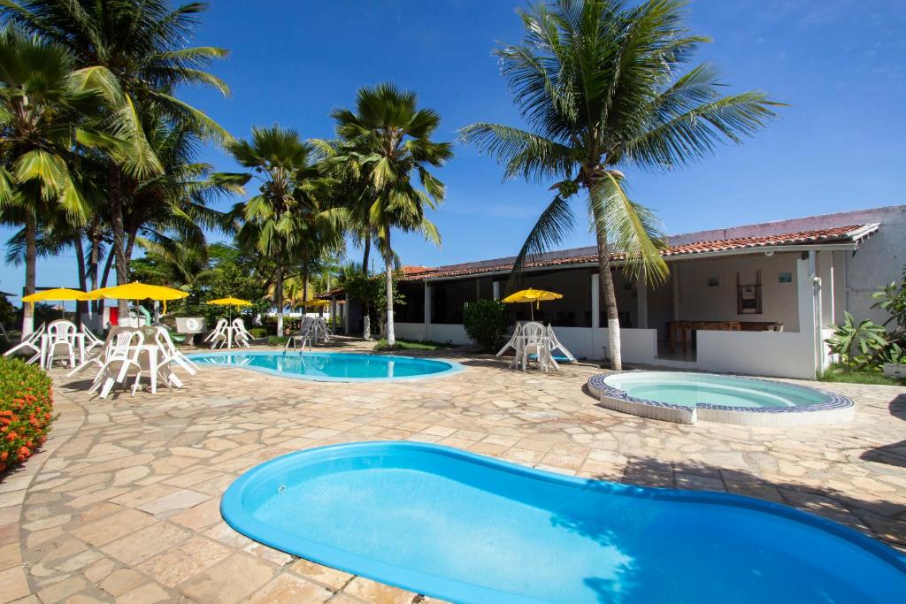 un complejo con 2 piscinas, sillas y palmeras en Pousada Do Inglês en Jacumã