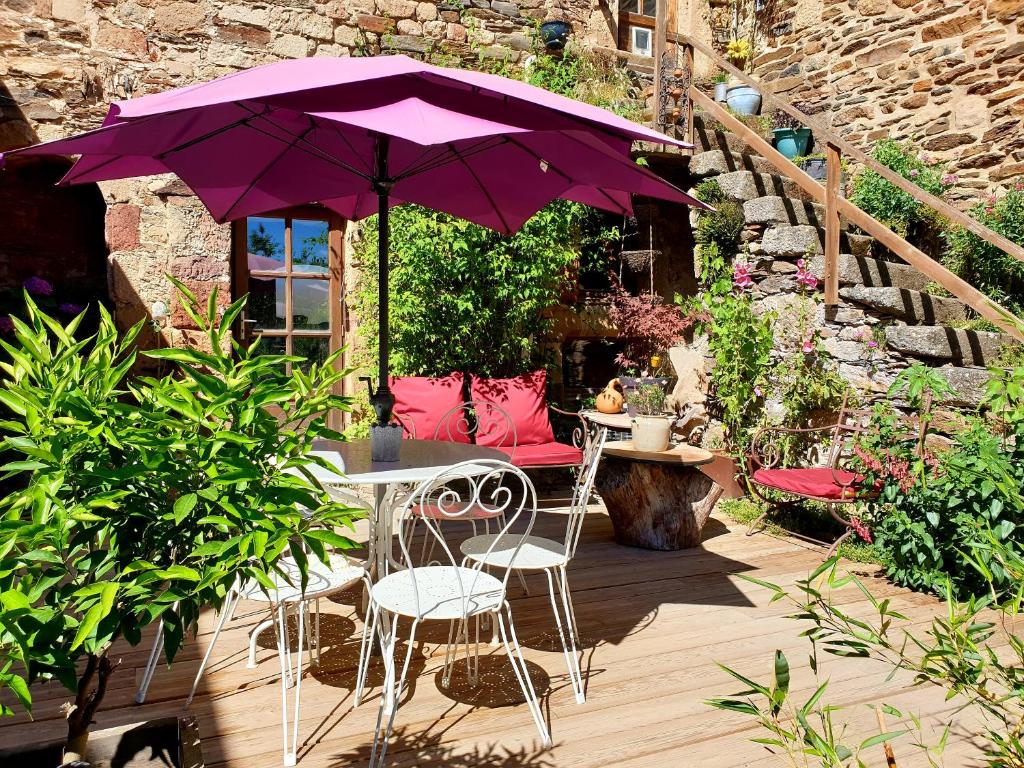 une terrasse avec un parasol violet, une table et des chaises dans l'établissement Gîte l'Echappée belle, à Castelnau-Pégayrols