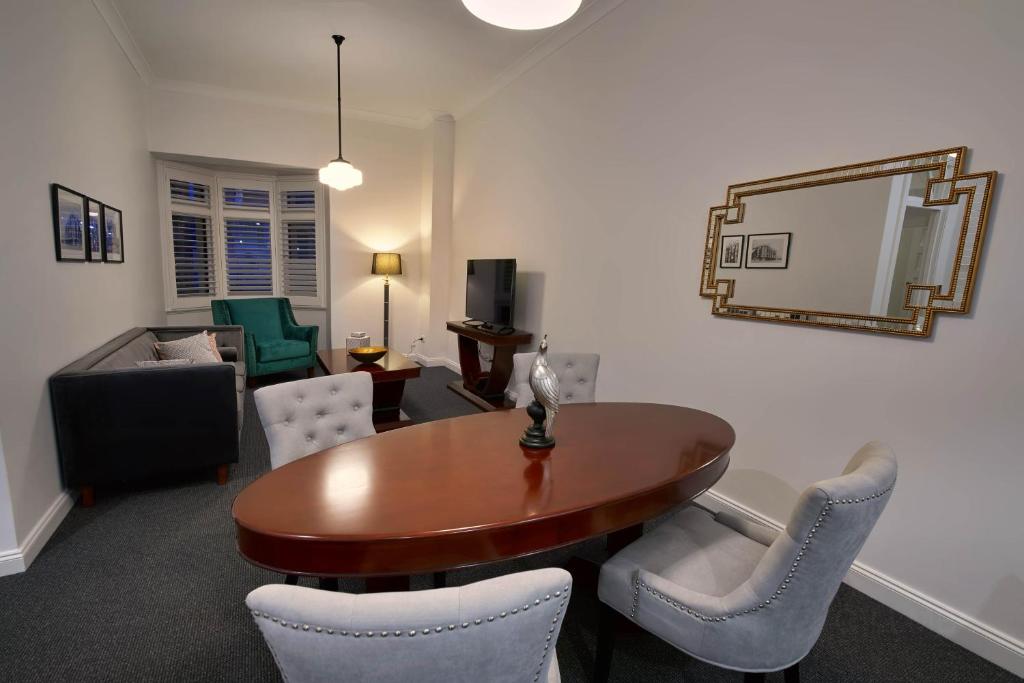 een woonkamer met een tafel en stoelen en een spiegel bij Mansions on Pulteney in Adelaide
