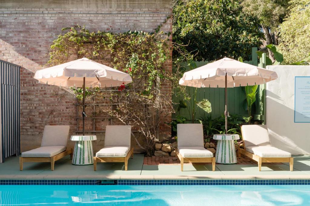 ein Pool mit zwei Sonnenschirmen und Stühlen neben einem Pool in der Unterkunft Palihouse Santa Barbara in Santa Barbara