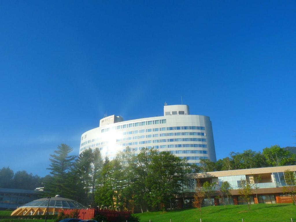 un gran edificio blanco con árboles delante de él en Shin Furano Prince Hotel, en Furano