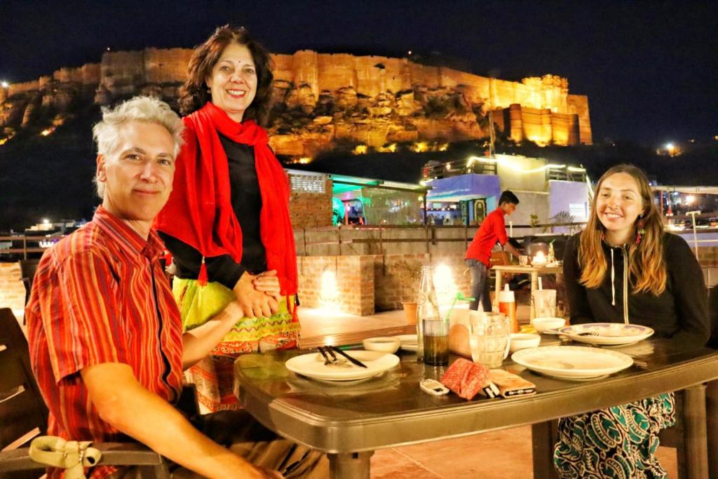 three people sitting at a table in front of a castle at Gopal Home Stay & Guest House in Jodhpur