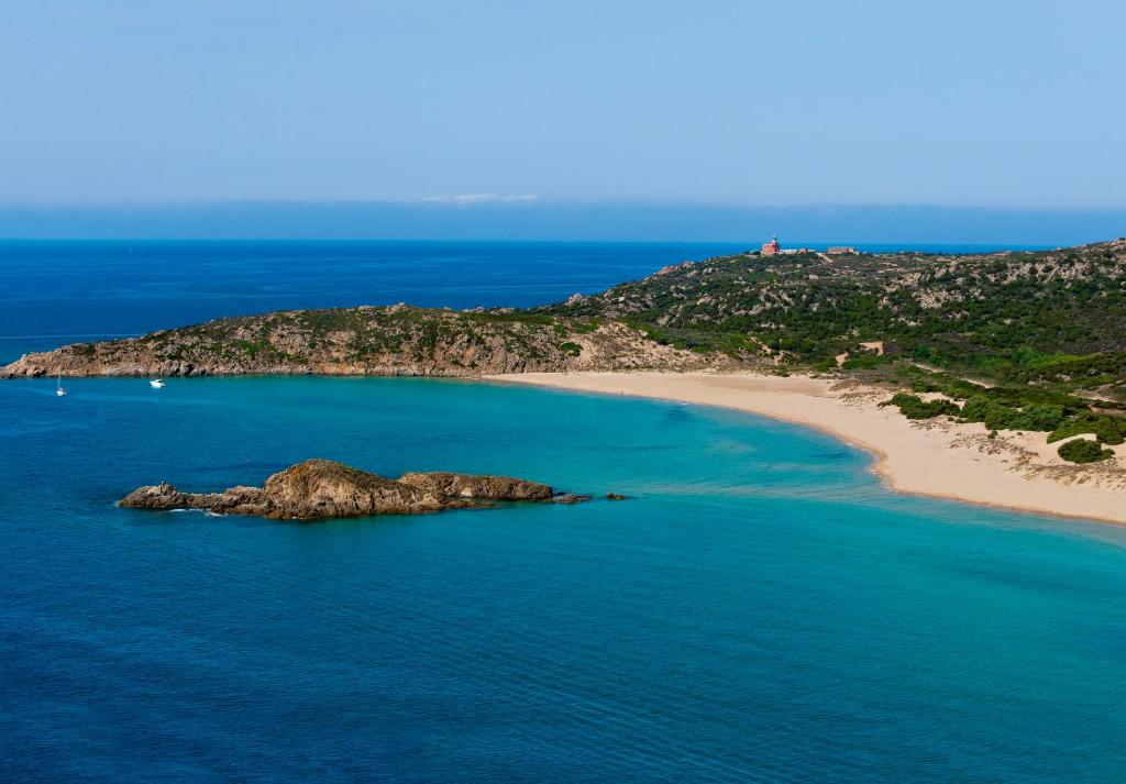 an island in the ocean next to a beach at Faro Capo Spartivento in Chia