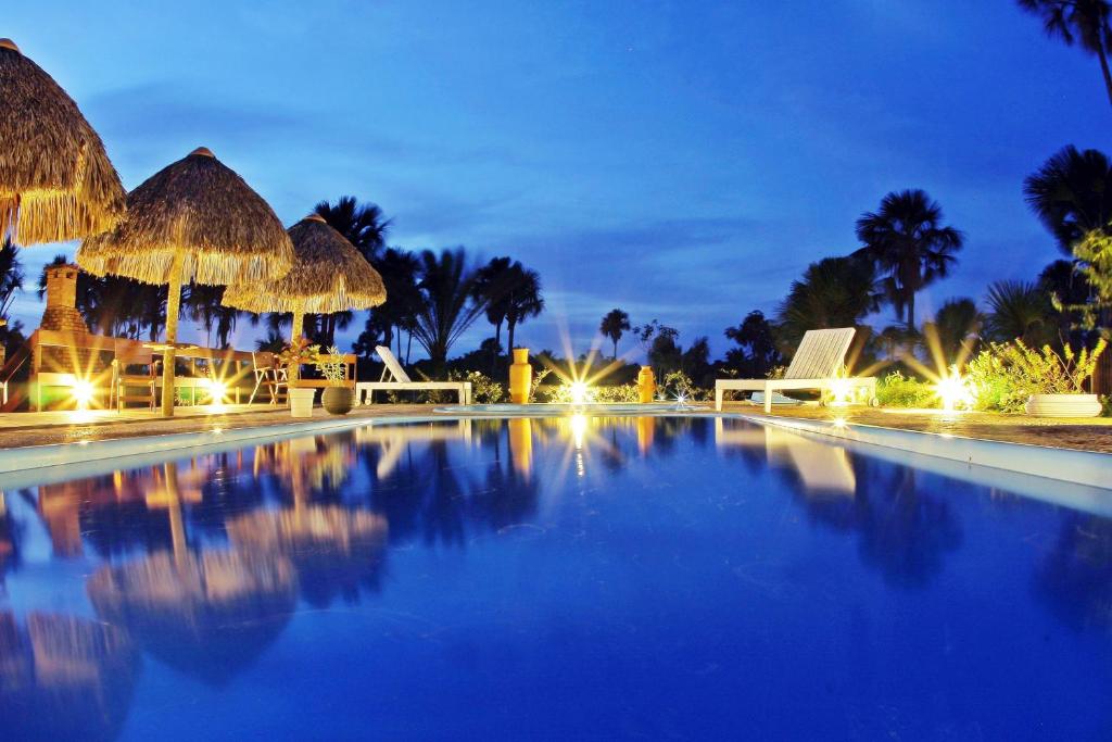 uma piscina à noite com cabanas e palmeiras em Encantes do Nordeste em Barreirinhas
