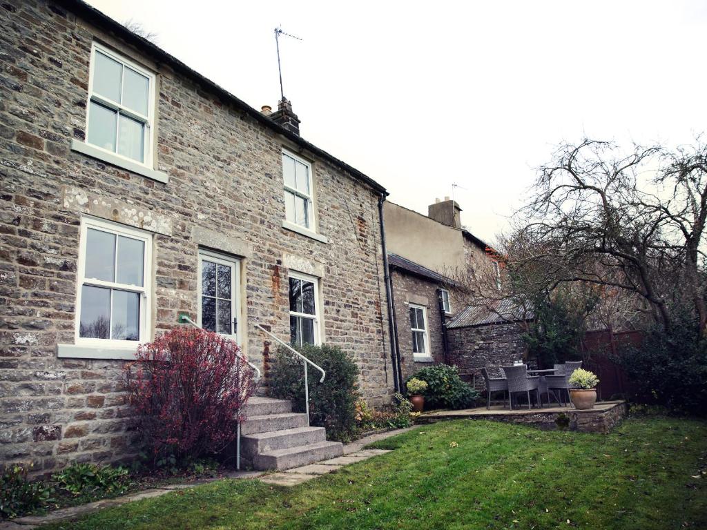 una casa de ladrillo con un patio de césped al lado de un edificio en West House, en Middleton in Teesdale