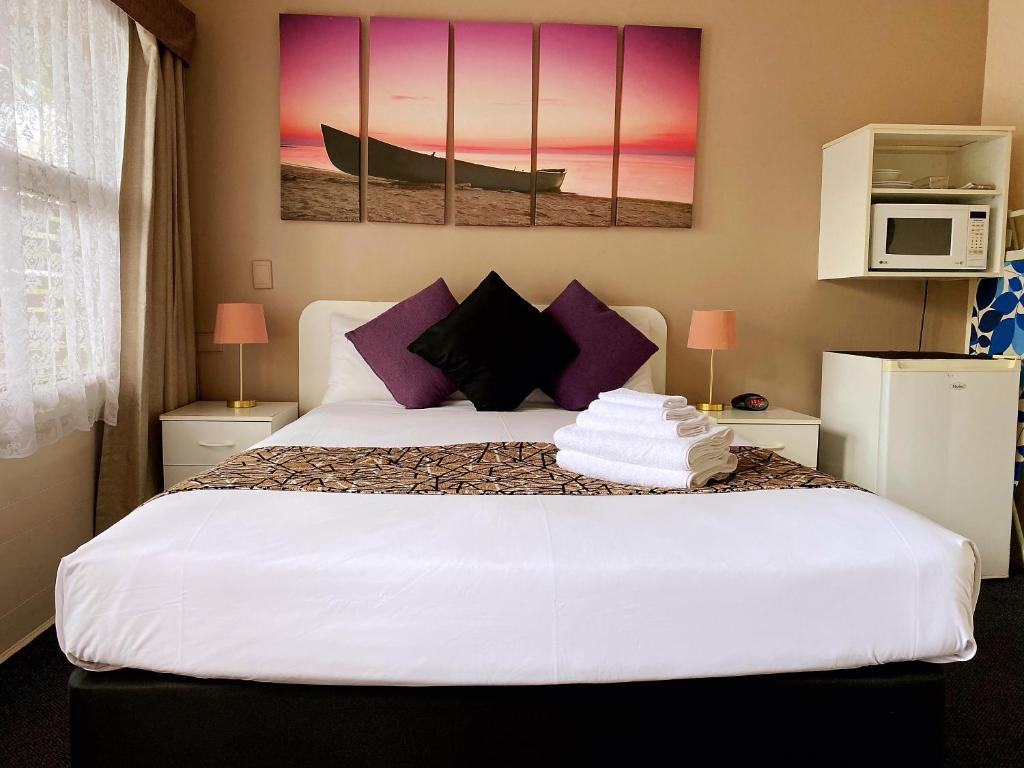 a bedroom with a large white bed with purple pillows at Motel Kempsey in Kempsey
