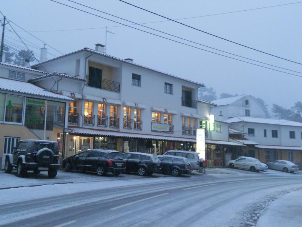 una calle nevada con coches aparcados frente a un edificio en Encosta da Serra, en Sabugueiro