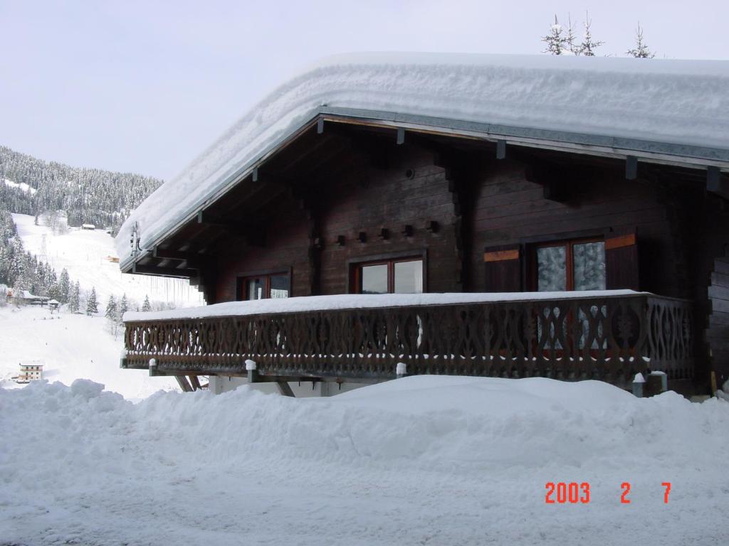 1 Authentique chalet, le Mirador في لي جيه: كابينة خشب مغطاة بالثلج مع شرفة