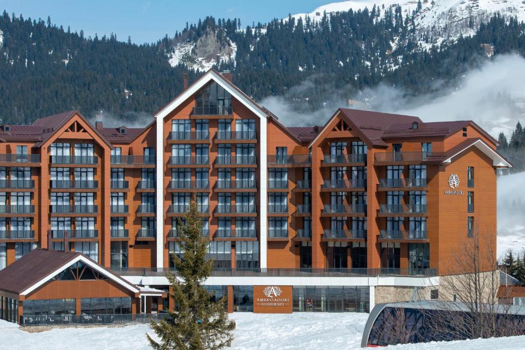 un gran edificio de apartamentos en la nieve con montañas en Ambassadori Goderdzi Hotel en Goderdzi