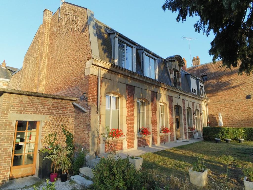 un vieux bâtiment en briques avec des fleurs rouges dans une cour dans l'établissement Chambres d'Hotes Noir Lion, à Péronne