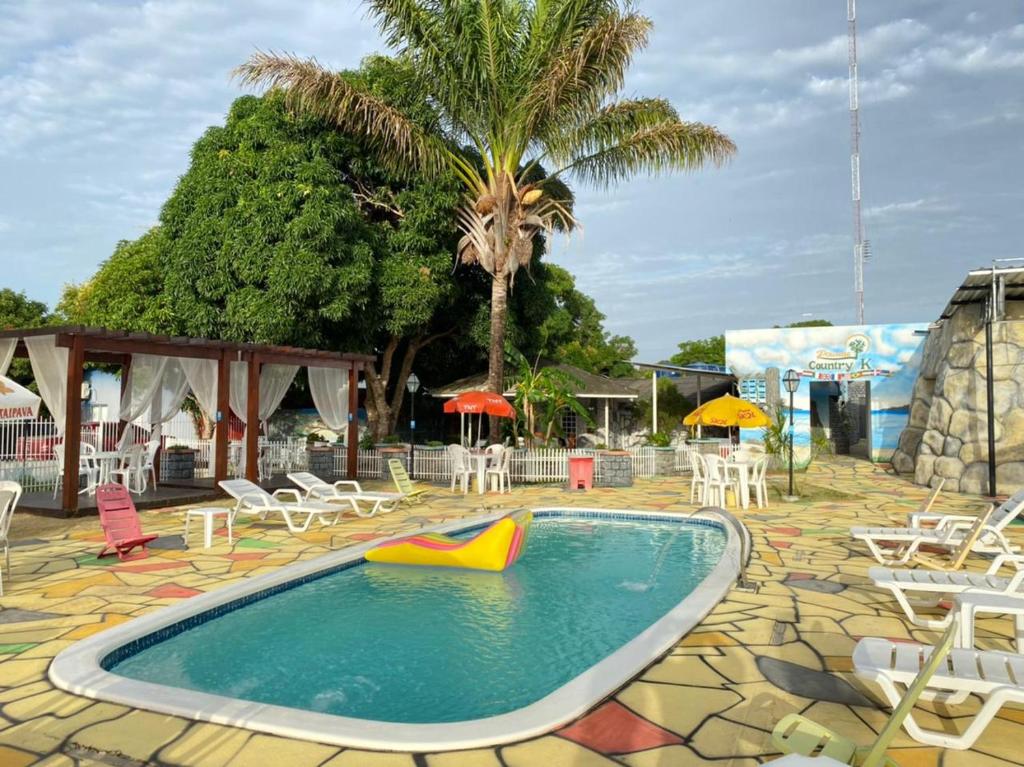 una piscina con sillas, mesas y una palmera en Pousada Country K en Boa Vista
