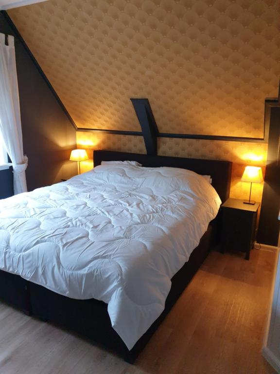 a bedroom with a large white bed with two lamps at Vakantiehuis Doelestee in Balk