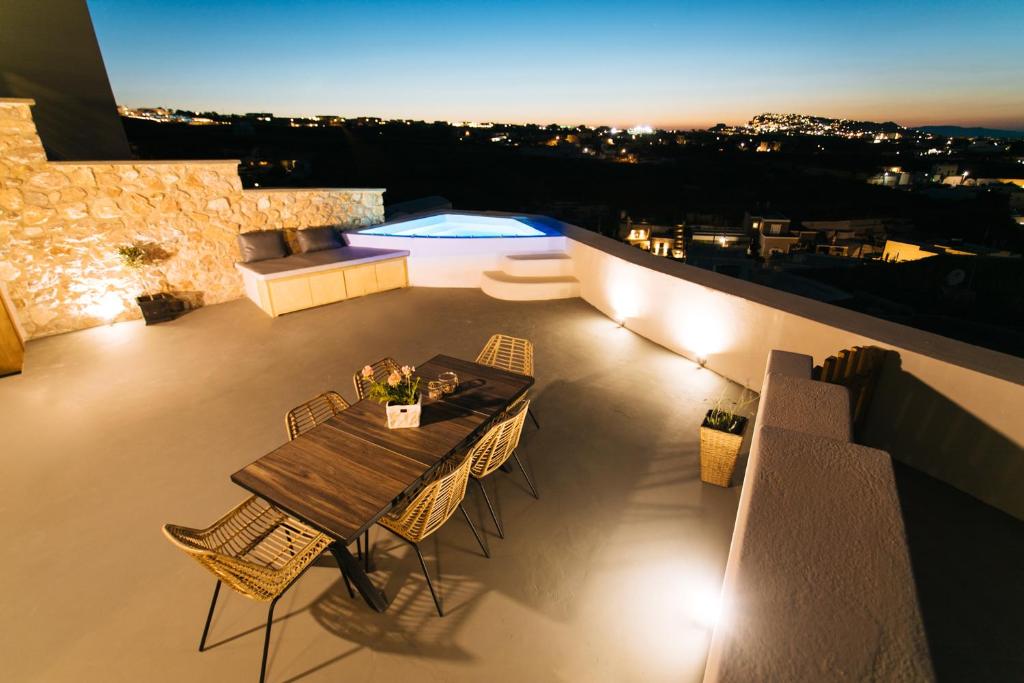Amer Villa Santorini with outdoor hot tub في Vóthon: طاولة طعام وكراسي على شرفة في الليل
