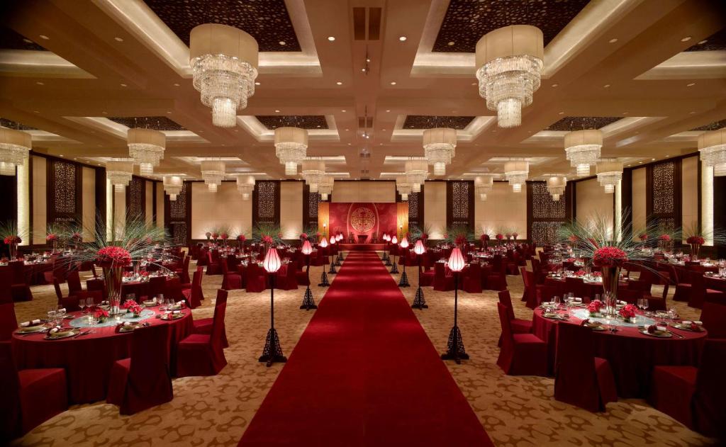 une salle de banquet avec des tables et des chaises rouges et un tapis rouge dans l'établissement Wyndham Grand Tianjin Jingjin City, à Tianjin