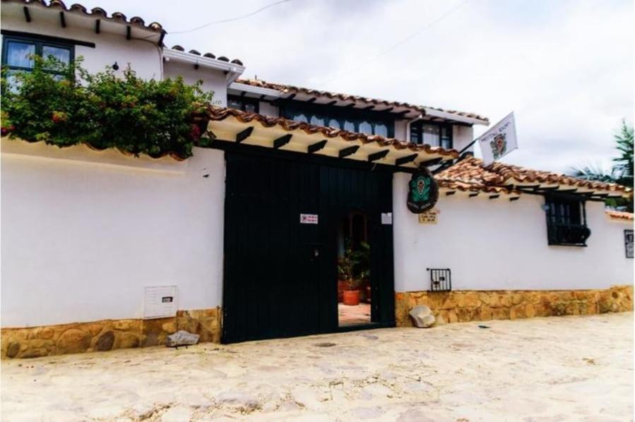 un edificio blanco con una puerta negra con techo en Hostal Rana en Villa de Leyva