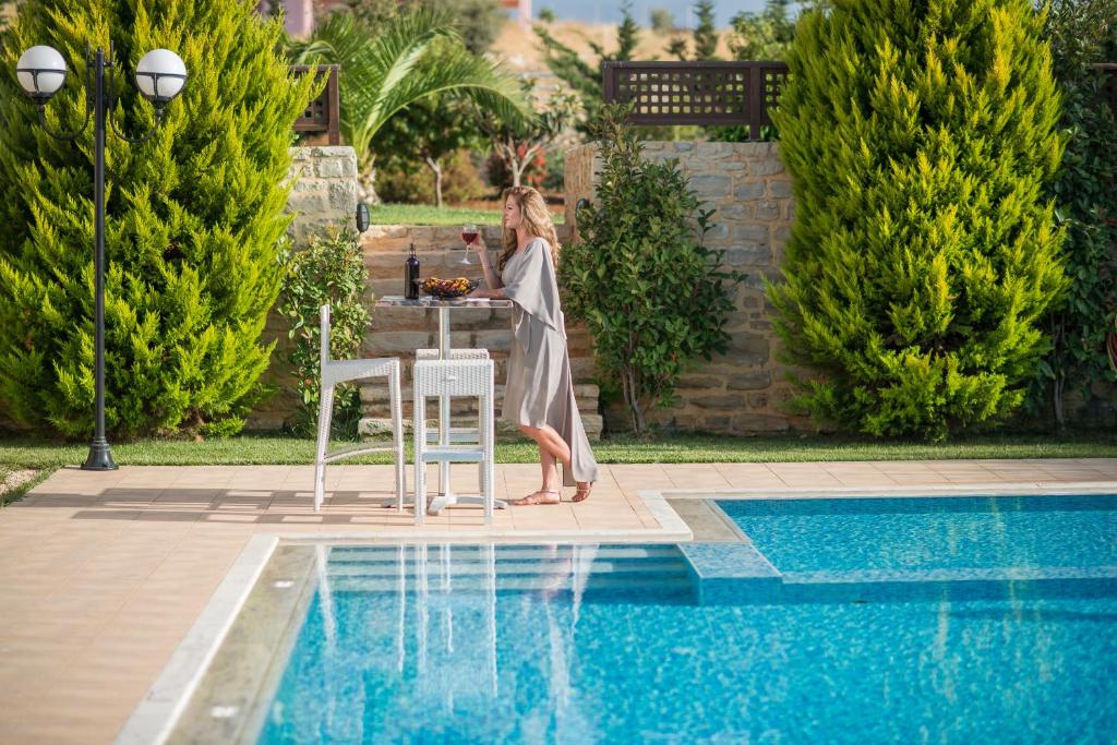 a woman standing at a table next to a pool at VILLA PASIFAI in Tria Monastiria