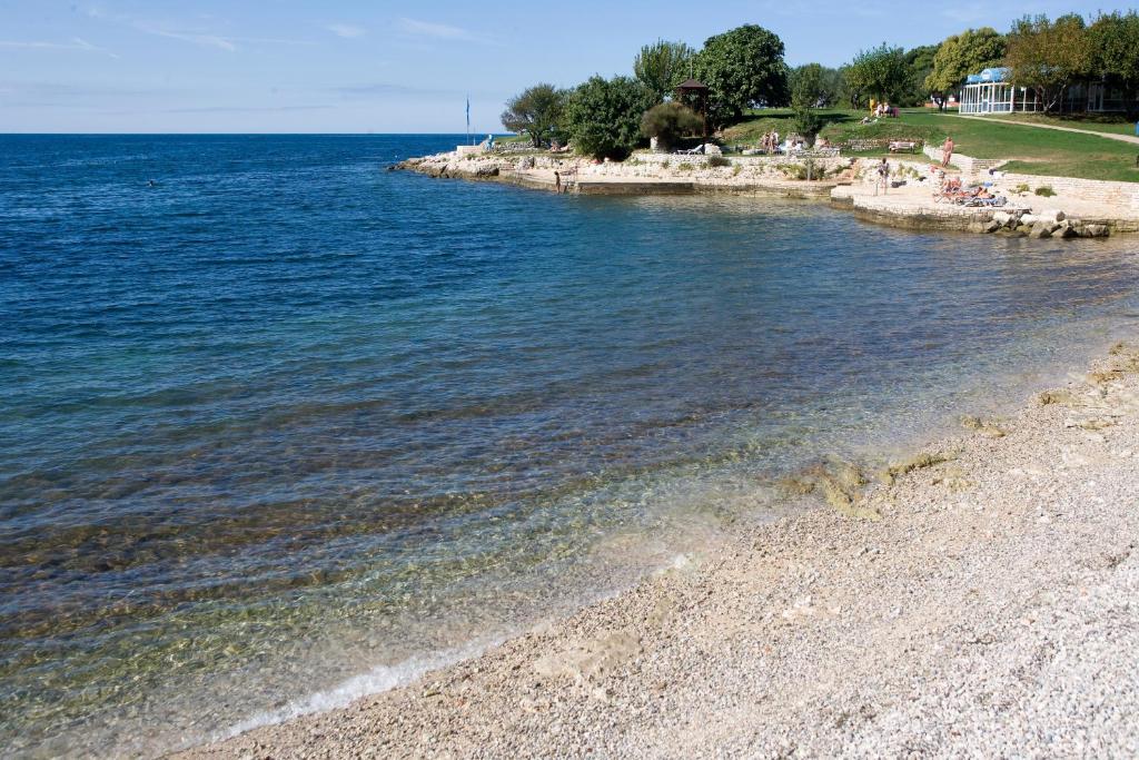 a beach with people sitting on the shore of the water at Hotel Albatros Plava Laguna in Poreč