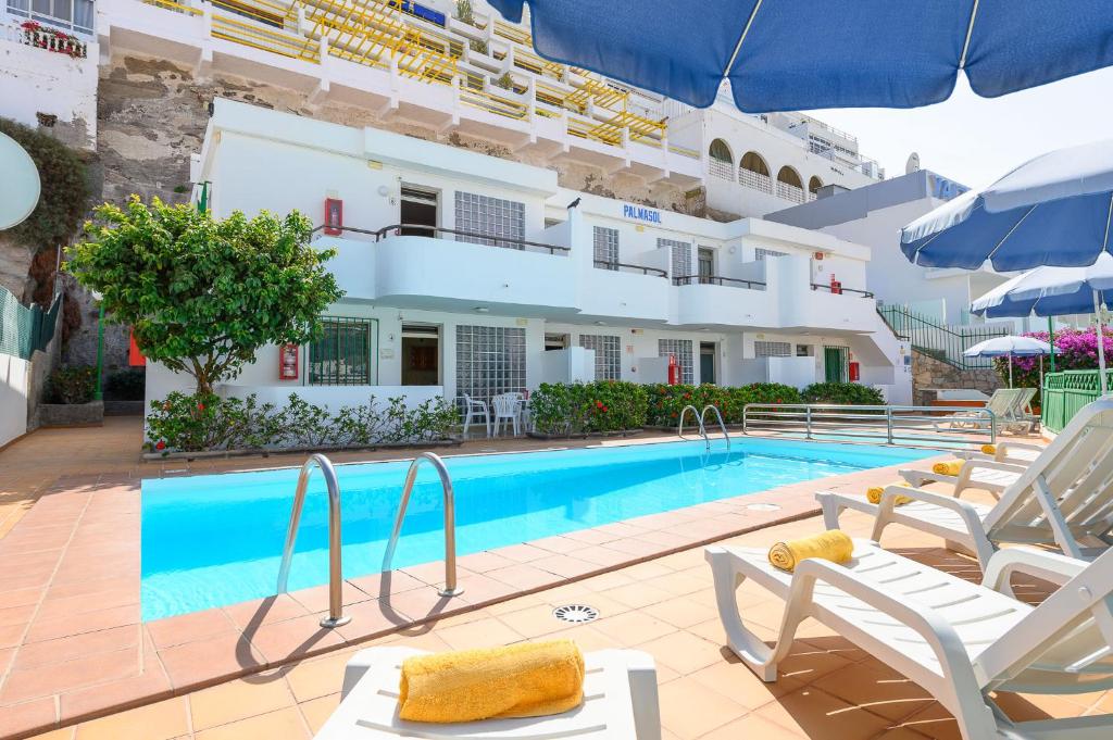 a swimming pool with chairs and a hotel at Palmasol Apartamentos in Puerto Rico de Gran Canaria